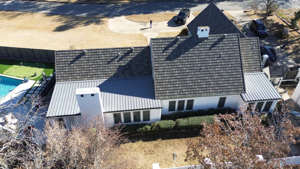 Aerial view of a white house with a dark roof and light gray paneled roof sections beside a backyard pool