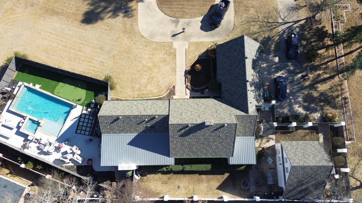 Top-down drone view of a home with a backyard pool, a dark roof and a light gray paneled porch roof