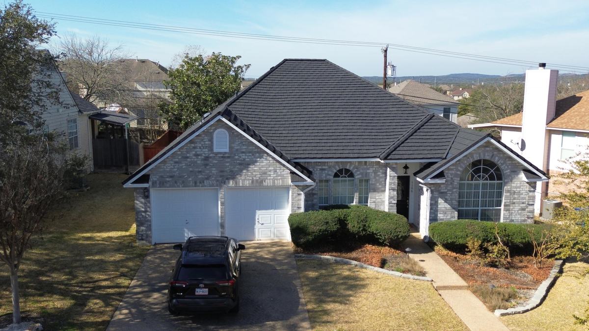 Drone view of the front of a single-story brick home with a charcoal roof and a two-car garage