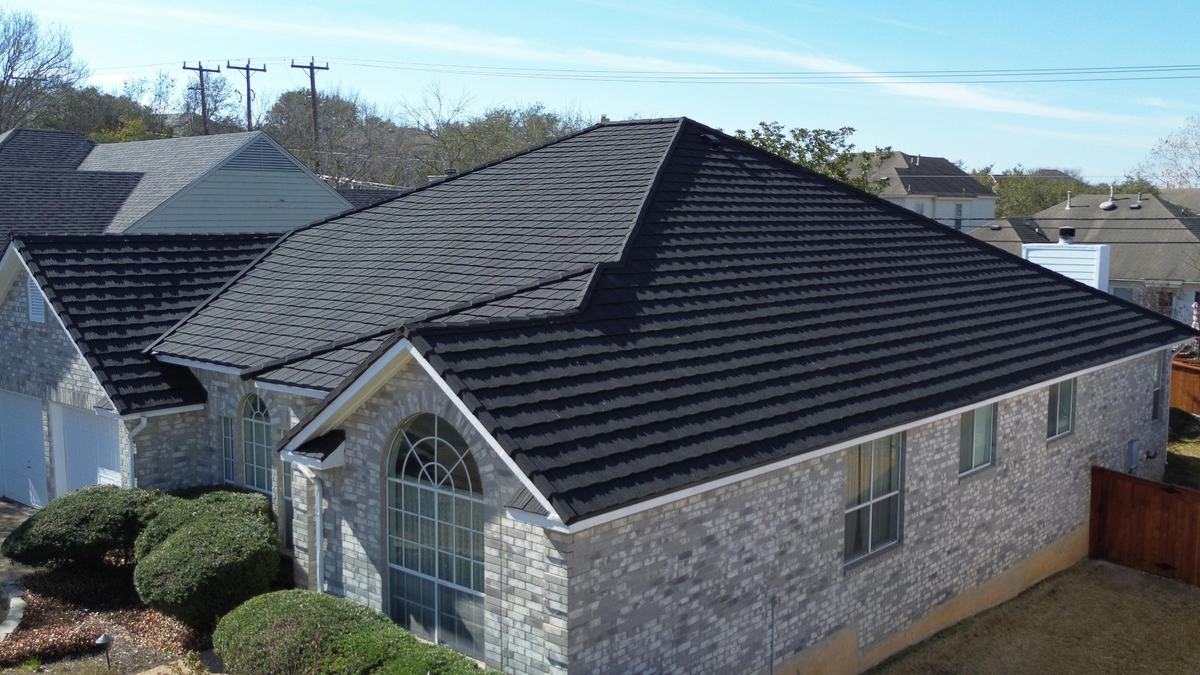 Drone view of a brick home with a hipped charcoal roof and an arched front window