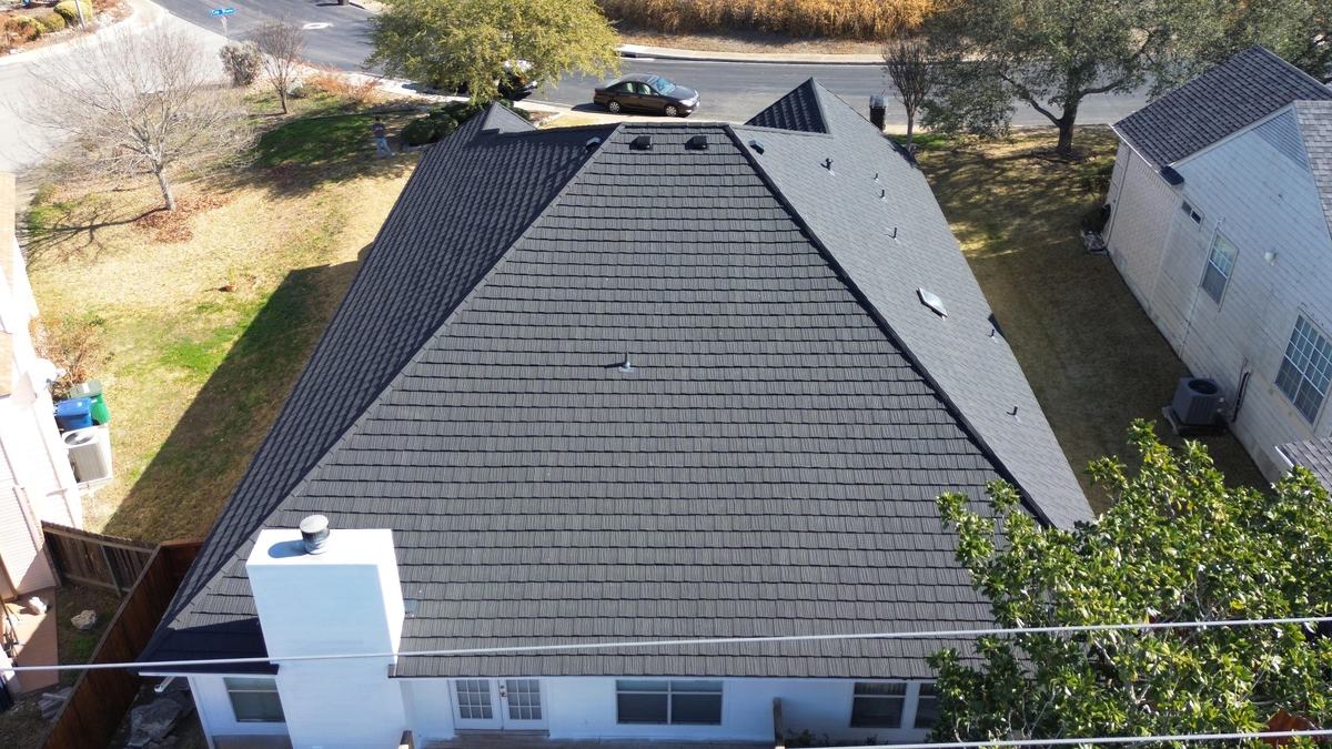 Overhead drone view of a charcoal roof and white chimney, looking toward the street